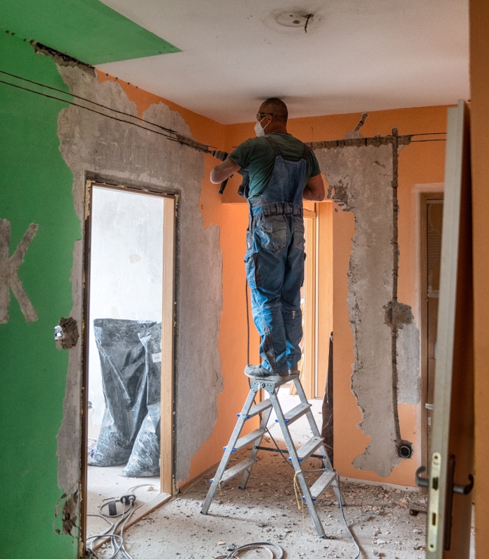 Ouvrier debout sur un escabeau en train de casser une cloison intérieure lors de travaux de rénovation